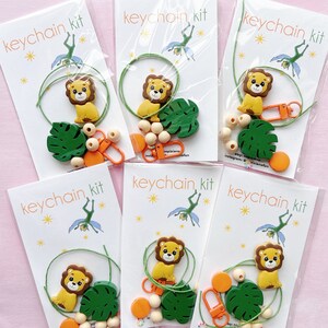 May include: A set of five DIY keychain kits featuring a lion, a green leaf, wooden beads, orange beads, and a string. Each kit comes with a card that says "keychain kit" and has a small illustration of a fairy.
