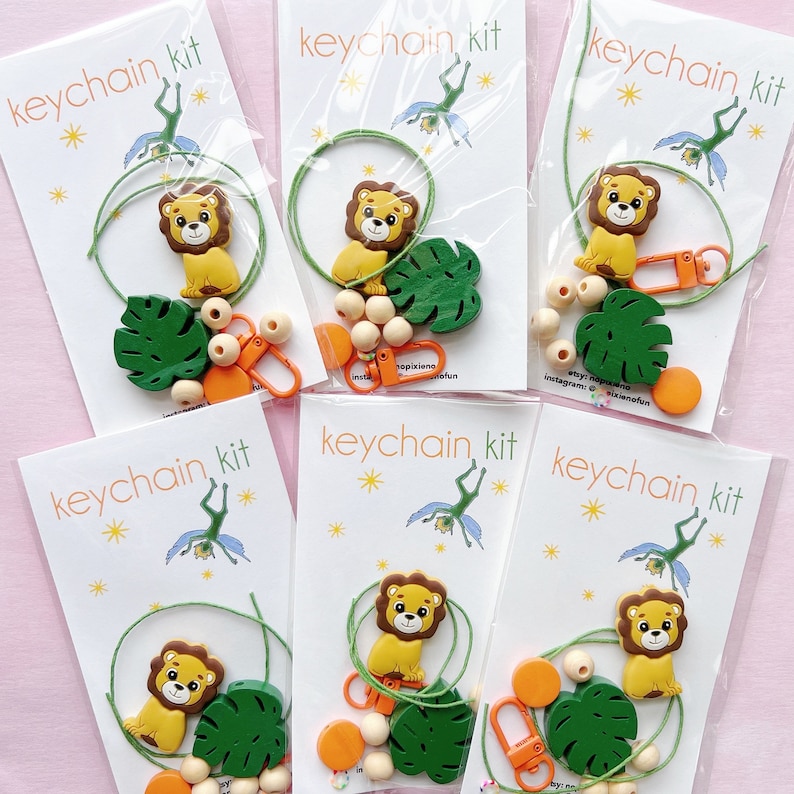 May include: A set of five DIY keychain kits featuring a lion, a green leaf, wooden beads, orange beads, and a string. Each kit comes with a card that says "keychain kit" and has a small illustration of a fairy.