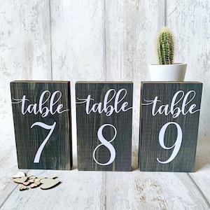 May include: Three rustic wooden table number signs with the words "table 7", "table 8", and "table 9" in white lettering.
