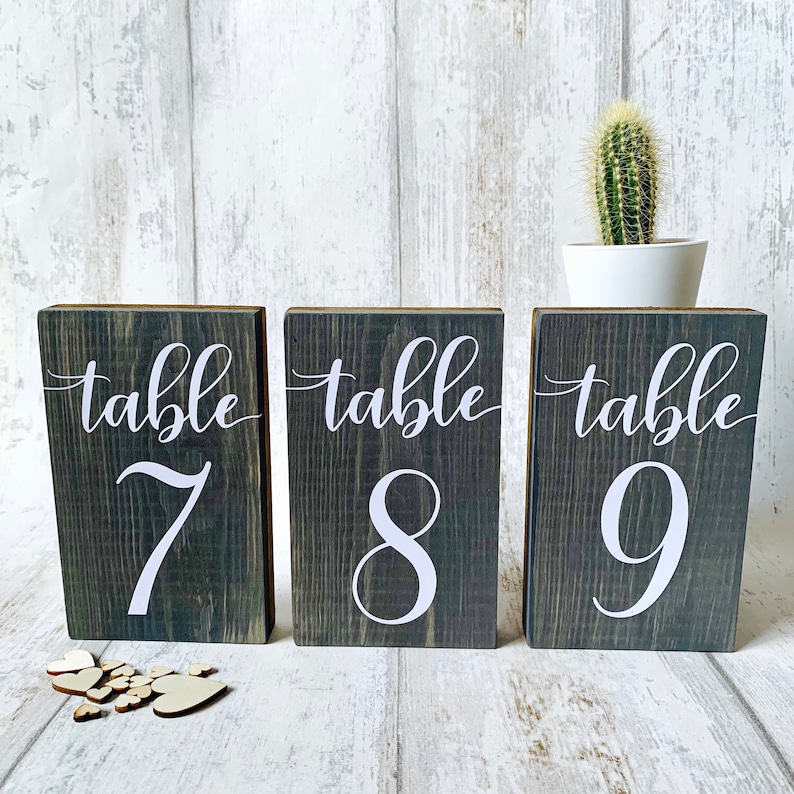 May include: Three rustic wooden table number signs with the words "table 7", "table 8", and "table 9" in white lettering.