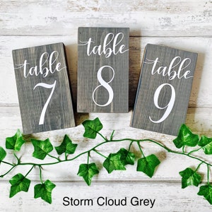 May include: Three wooden table number signs with the words "table" and the numbers 7, 8, and 9 in white paint. The signs are painted in a dark gray color called "Storm Cloud Grey".