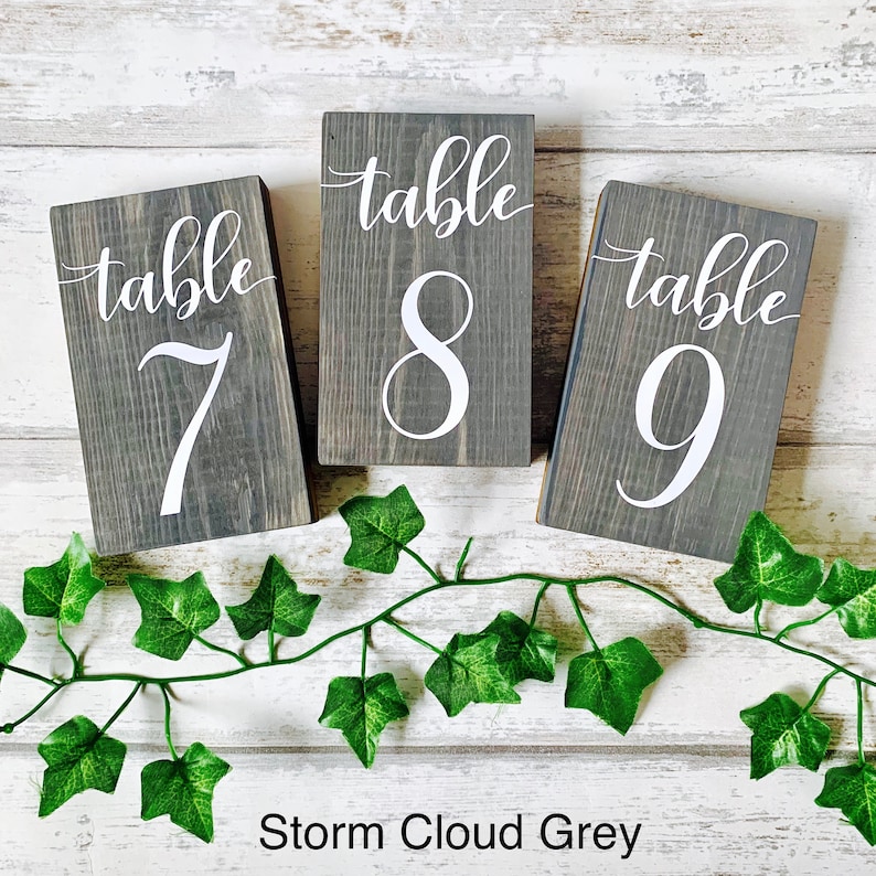 May include: Three wooden table number signs with the words "table" and the numbers 7, 8, and 9 in white paint. The signs are painted in a dark gray color called "Storm Cloud Grey".