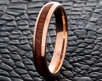 Puede incluir: Un anillo de oro rosa con una incrustación de madera marrón oscuro. El anillo tiene un acabado pulido, que resalta el contraste entre el metal y la veta de la madera. El anillo es de diseño sencillo.