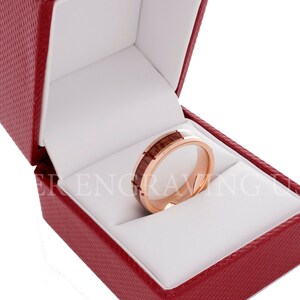 May include: A rose gold wedding band with a wood inlay in a red velvet ring box.