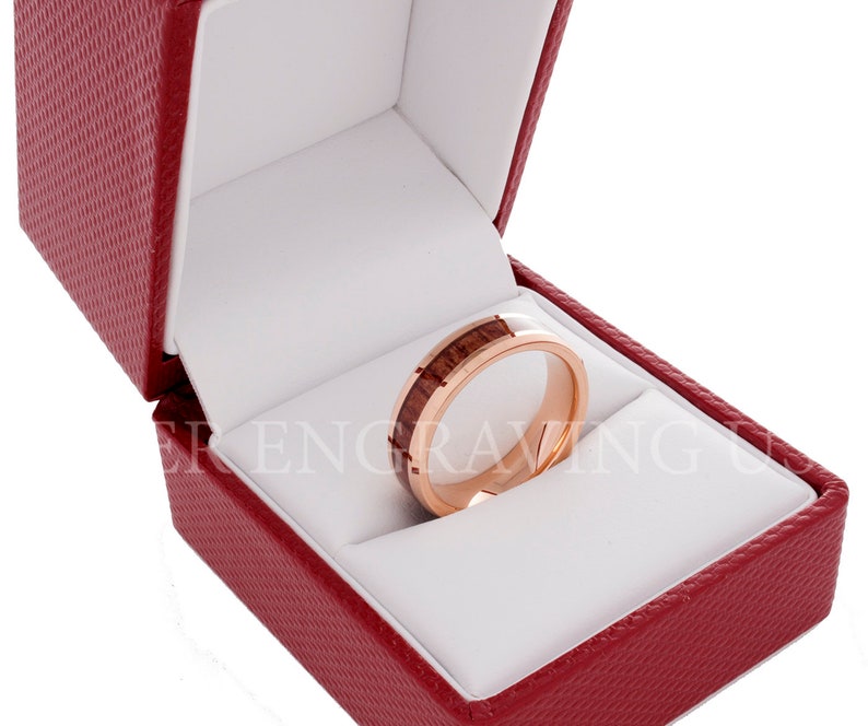 May include: A rose gold wedding band with a wood inlay in a red velvet ring box.