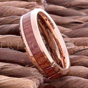 May include: A rose gold tungsten carbide ring with a wooden inlay. The ring has a beveled edge and a polished finish.