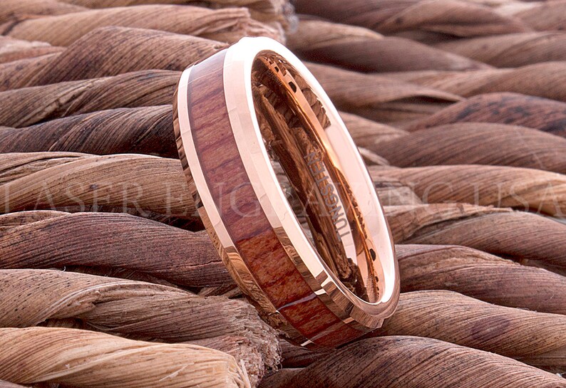 May include: A rose gold tungsten carbide ring with a wooden inlay. The ring has a beveled edge and a polished finish.