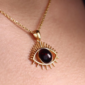 May include: A gold chain necklace with a pendant shaped like an eye. The eye is made of a dark red gemstone.