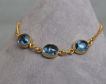 May include: A gold chain bracelet with three oval-shaped blue gemstones.