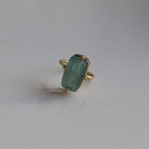 May include: A gold ring with a light blue, rectangular gemstone set in a bezel setting.