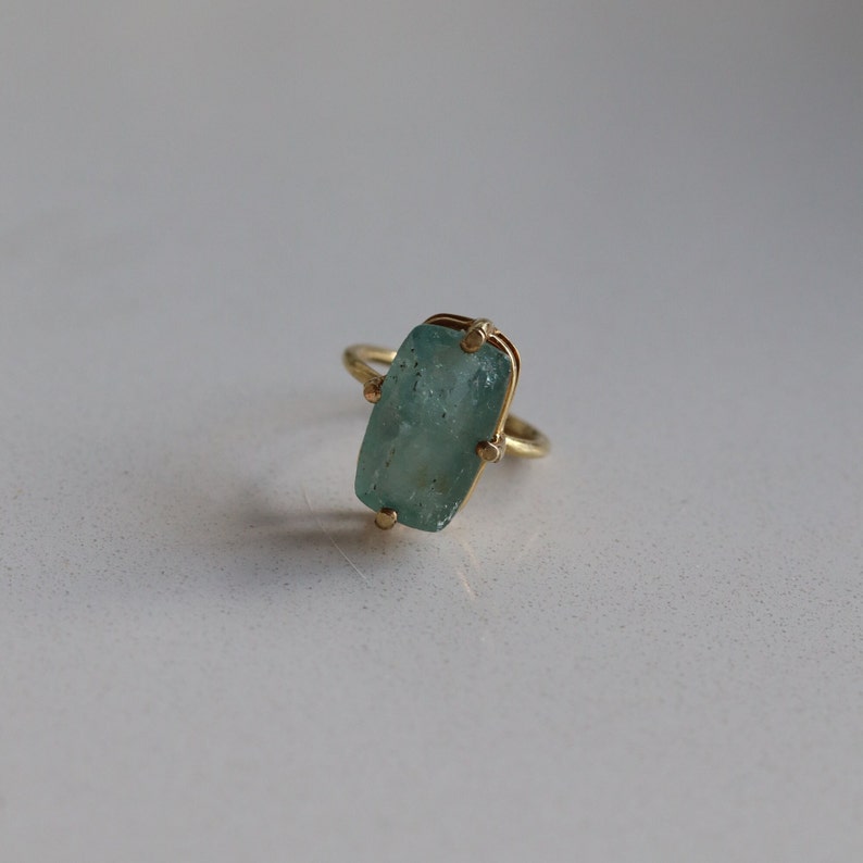 May include: A gold ring with a light blue, rectangular gemstone set in a bezel setting.