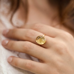 Puede incluir: Un anillo de oro con una piedra redonda de color amarillo claro engastada en el centro.