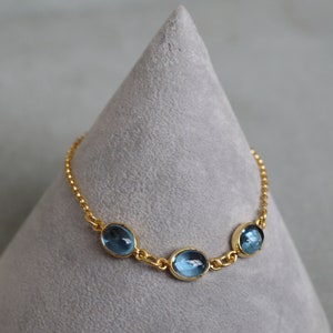 May include: A gold chain bracelet with three oval-shaped blue gemstones.