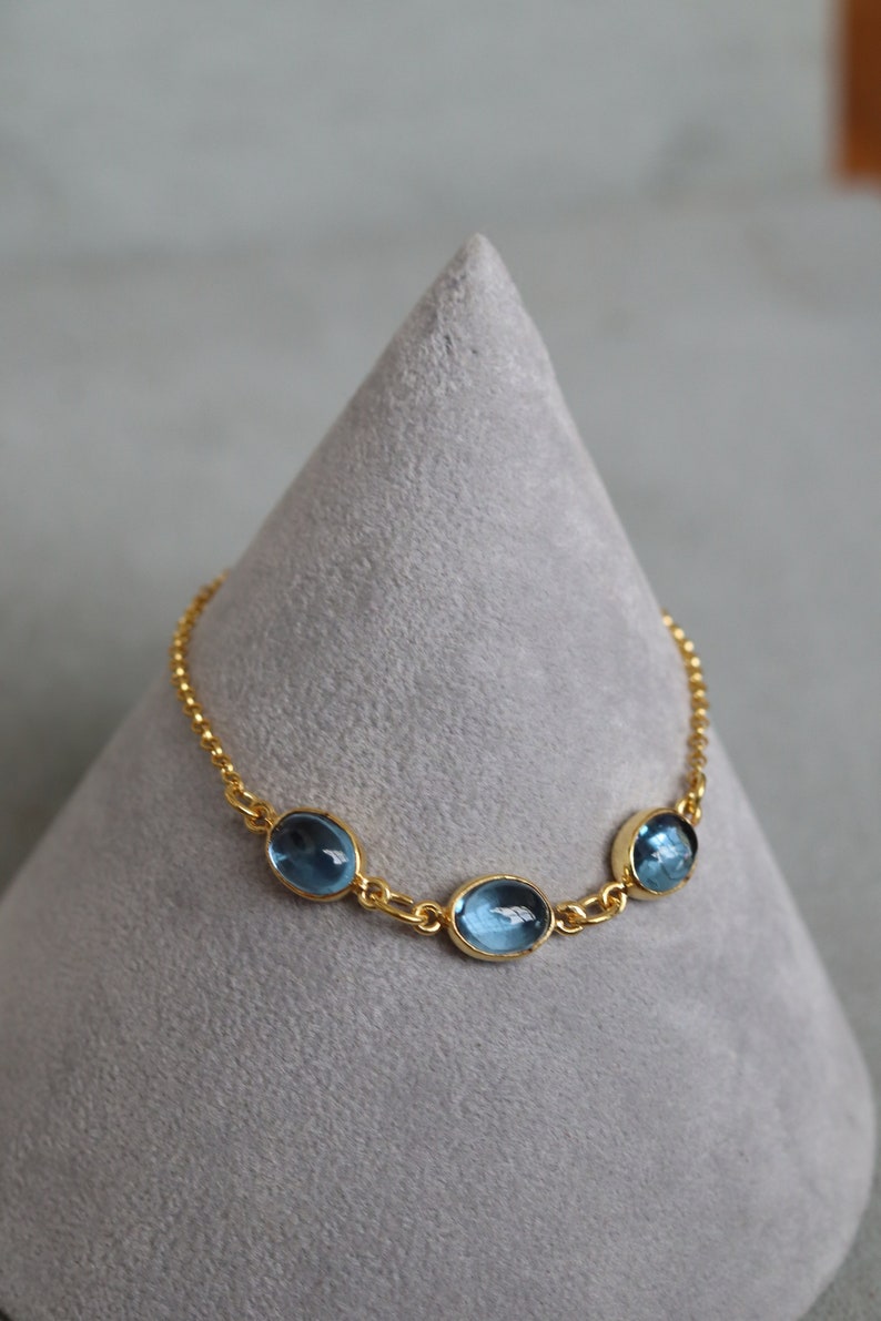 May include: A gold chain bracelet with three oval-shaped blue gemstones.