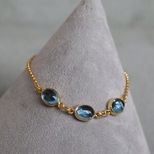 May include: A gold chain bracelet with three oval-shaped blue gemstones.