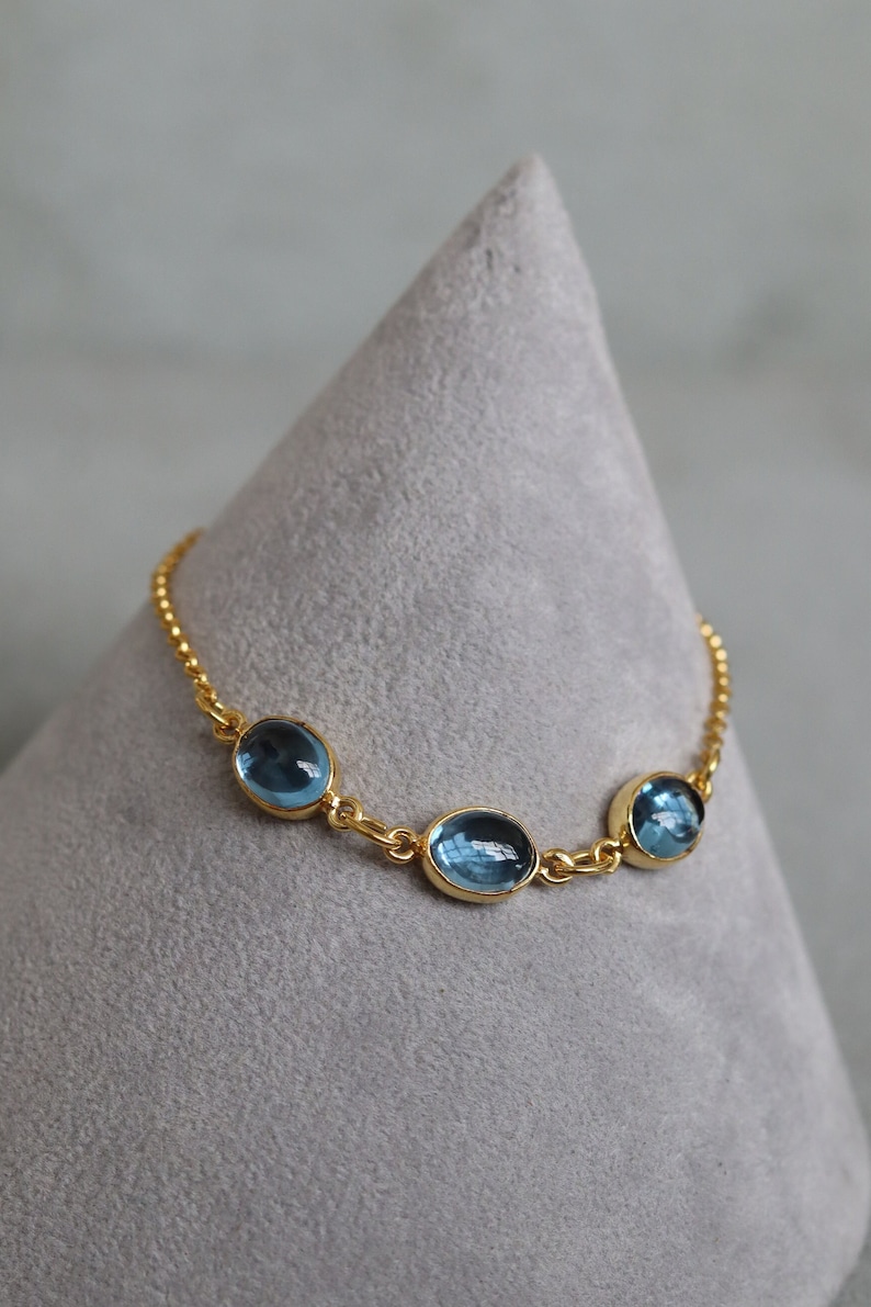 May include: A gold chain bracelet with three oval-shaped blue gemstones.