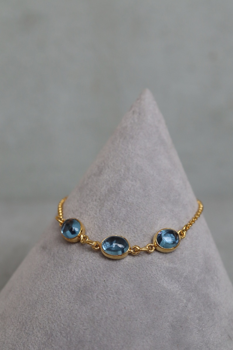 May include: A gold chain bracelet with three oval-shaped blue gemstones.