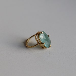 May include: A gold ring featuring a large, light blue gemstone set in a geometric design.