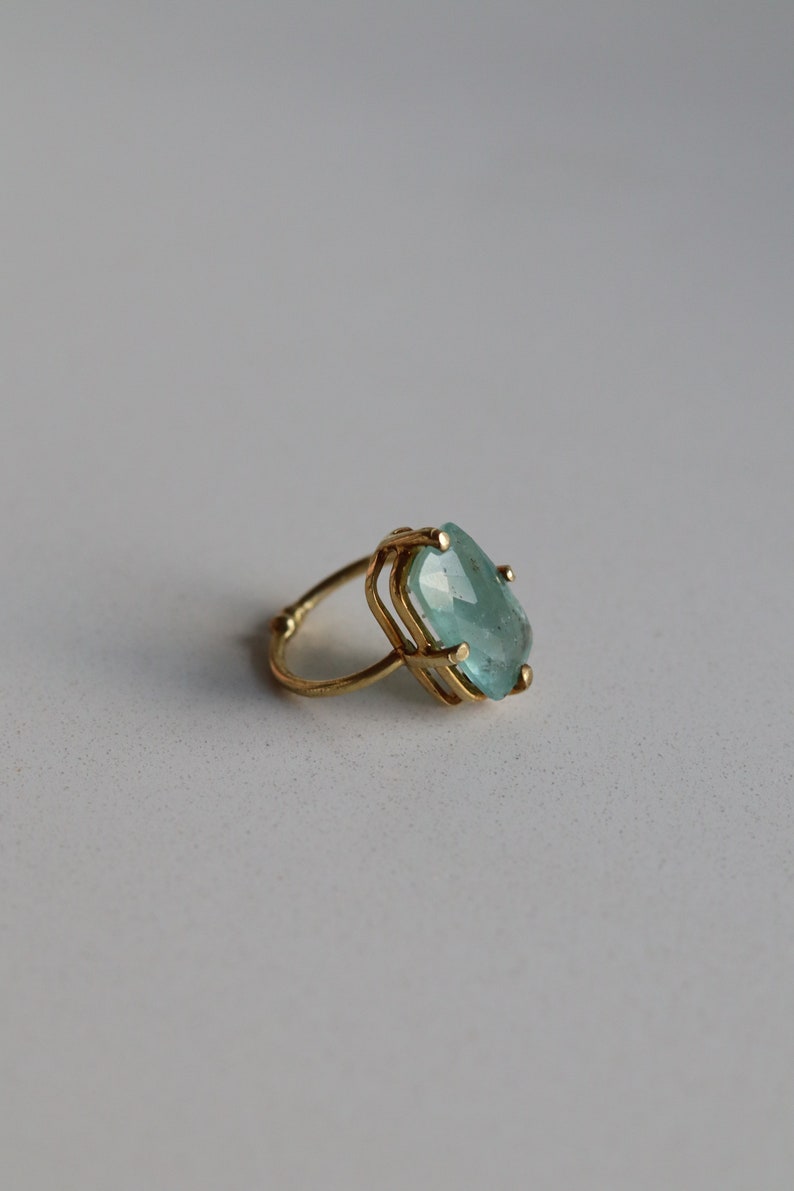 May include: A gold ring featuring a large, light blue gemstone set in a geometric design.