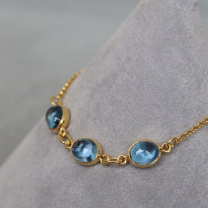 May include: A gold chain bracelet with three oval-shaped blue gemstones.