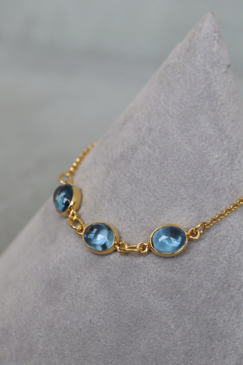 May include: A gold chain bracelet with three oval-shaped blue gemstones.