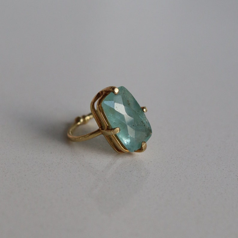 May include: A gold ring featuring a light blue gemstone. The gemstone is rectangular in shape with facets.
