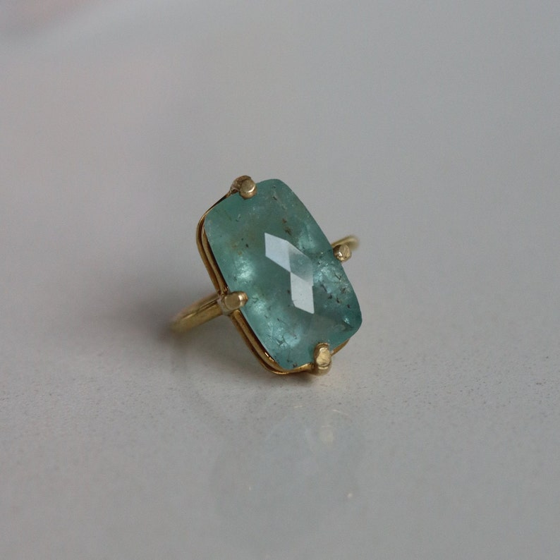 May include: A gold ring featuring a large, rectangular, light blue gemstone.