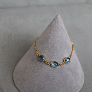 May include: A gold chain bracelet with three oval-shaped blue gemstones.