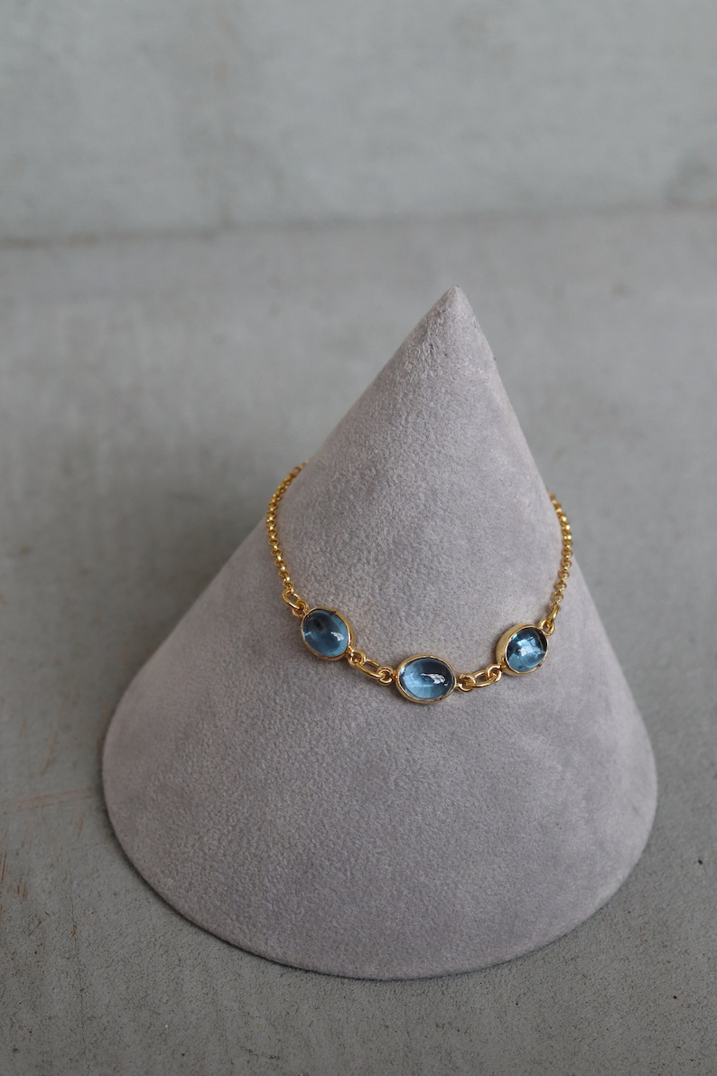 May include: A gold chain bracelet with three oval-shaped blue gemstones.