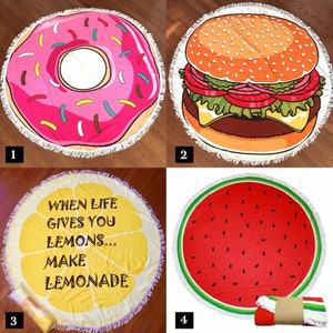 May include: Four round beach towels with different designs. The first towel features a pink and white donut with pink sprinkles. The second towel features a cartoon burger with lettuce, tomato, cheese, and a sesame seed bun. The third towel is yellow with a lemon slice and the text "When life gives you lemons... make lemonade". The fourth towel is red and green with a watermelon design.