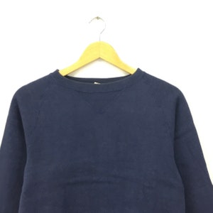May include: A navy blue sweatshirt with a crew neck and long sleeves. The sweatshirt is hanging on a wooden hanger.