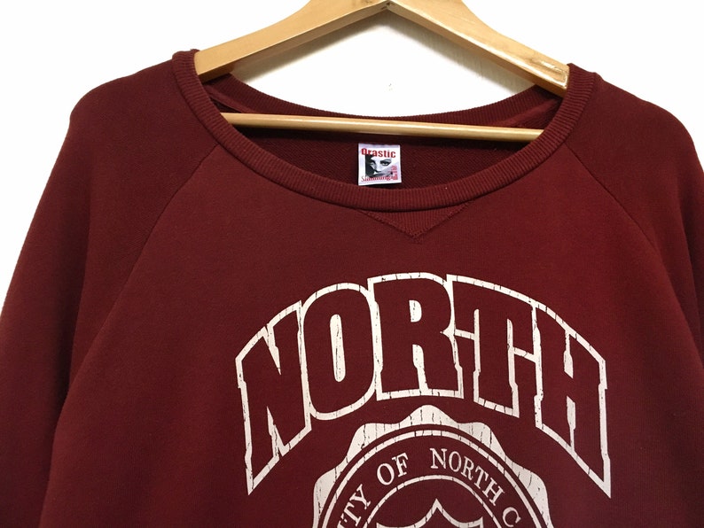 May include: Burgundy red sweatshirt with a white graphic of the word "NORTH" in a vintage style font. The graphic also includes a circular design with the text "University of North Carolina".