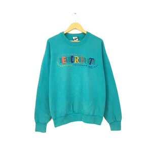 May include: Teal blue sweatshirt with a colorful graphic print of the word "EVERETT" in a circle with the text "WESTERN REGIONAL" above and "WISCONSIN NOISE" below.