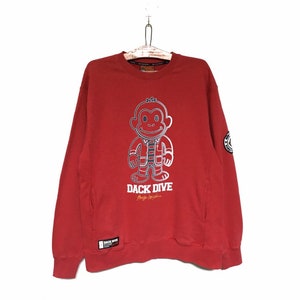 May include: Red sweatshirt with a cartoon monkey wearing a jacket and the text "DACK DIVE" printed on the front.