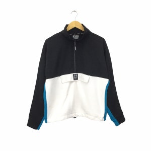 May include: Black and white quarter-zip sweatshirt with a blue accent. The sweatshirt has a pocket on the front with the text "DKNY" printed on it.