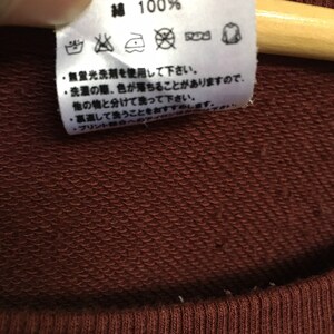 May include: A close-up of a brown care tag with white text and symbols. The tag says "Cotton 100%" and includes instructions for washing, bleaching, ironing, and drying.