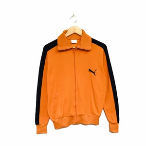 May include: Orange and black vintage Puma track jacket with a zipper closure and black side panels.