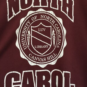 May include: White text on a maroon background reads "NORTH" in a large font, followed by a circular seal with the text "UNIVERSITY OF NORTH CAROLINA CANVAS HILL LIBRARY" and a shield with the text "LUV" inside. The text "CAROL" is below the seal in a large font.