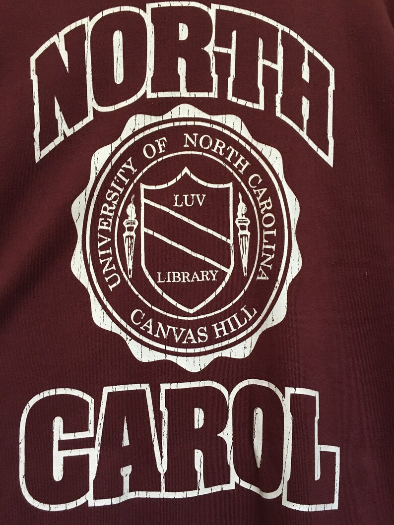 May include: White text on a maroon background reads "NORTH" in a large font, followed by a circular seal with the text "UNIVERSITY OF NORTH CAROLINA CANVAS HILL LIBRARY" and a shield with the text "LUV" inside. The text "CAROL" is below the seal in a large font.