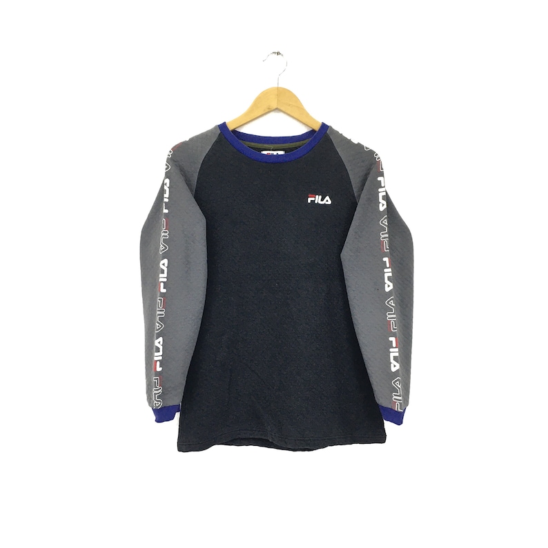 May include: A gray and black long-sleeve shirt with the word "FILA" printed on the front. The sleeves have a gray and white stripe pattern with the word "FILA" repeated.