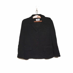 Peut inclure: Un blazer noir avec une fermeture à bouton unique et deux poches. Le blazer porte une étiquette indiquant "Collezione".