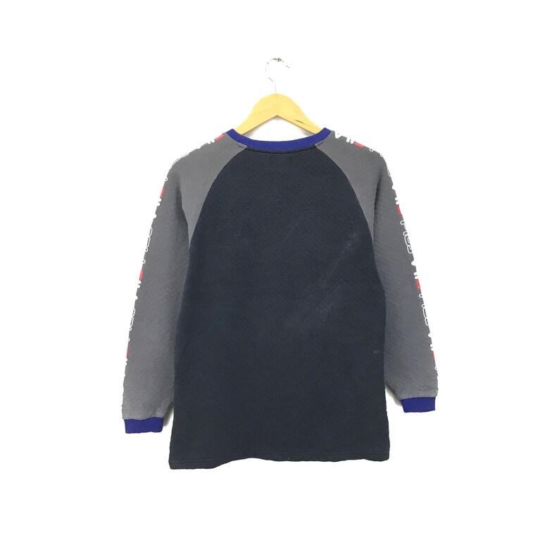 May include: A long-sleeved, navy blue and gray sweatshirt with a white and red print on the sleeves. The sweatshirt has a crew neck and a raglan sleeve design.