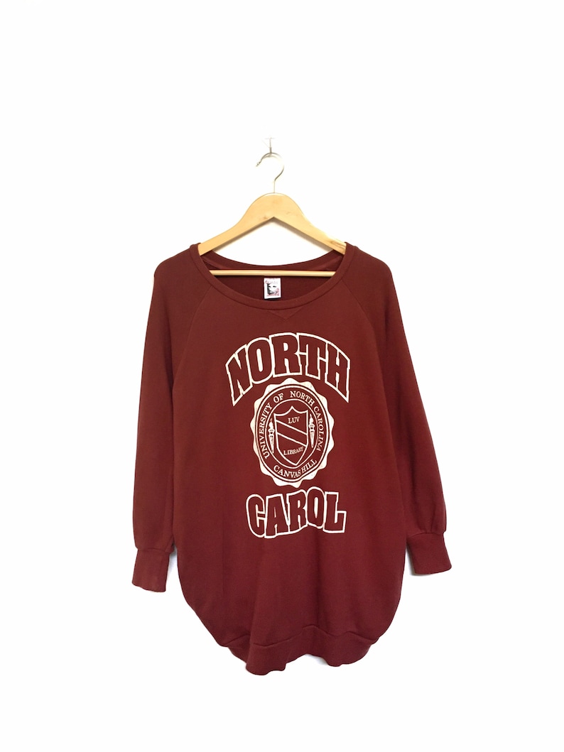 May include: A maroon sweatshirt with a white graphic of the University of North Carolina at Chapel Hill logo and the word "NORTH CAROL" in a white outline.