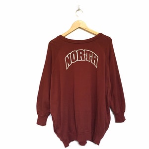 May include: A maroon sweatshirt with a white "NORTH" graphic on the back. The sweatshirt has a crew neck and long sleeves.