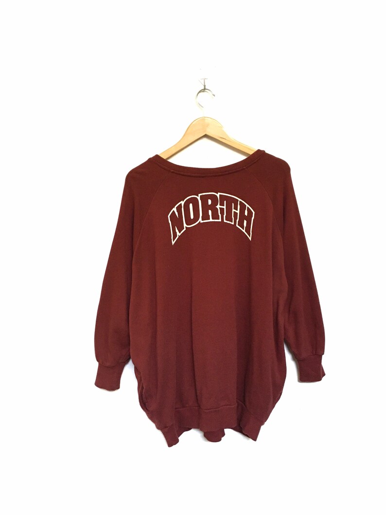 May include: A maroon sweatshirt with a white "NORTH" graphic on the back. The sweatshirt has a crew neck and long sleeves.