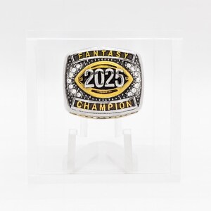 Puede incluir: Un anillo de campeonato de f&uacute;tbol fant&aacute;stico plateado y dorado. El anillo presenta el a&ntilde;o "2025" en el centro, rodeado por una forma de bal&oacute;n de f&uacute;tbol dorada. Las palabras "FANTASY" y "CHAMPION" est&aacute;n inscritas en el anillo.