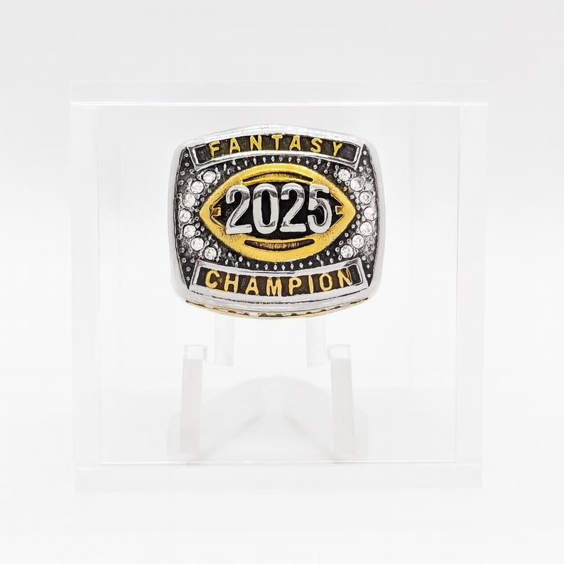Puede incluir: Un anillo de campeonato de f&uacute;tbol fant&aacute;stico plateado y dorado. El anillo presenta el a&ntilde;o "2025" en el centro, rodeado por una forma de bal&oacute;n de f&uacute;tbol dorada. Las palabras "FANTASY" y "CHAMPION" est&aacute;n inscritas en el anillo.