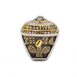 May include: A gold and silver football championship ring with the year 2024 displayed. The ring features the words "FOOTBALL WIN" and is adorned with numerous clear gemstones. The design includes a football and the number 24.