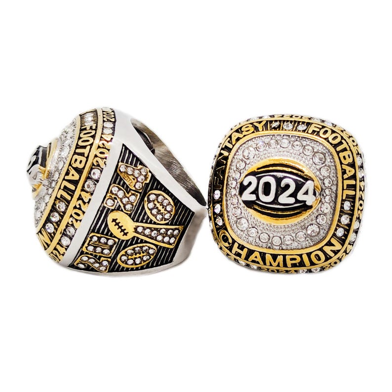 May include: Two fantasy football championship rings. One ring is angled, showing the side with the text "2024 FOOTBALL CHAMPION". The other ring is face-up, displaying "2024" and "CHAMPION" in gold lettering, surrounded by clear stones.