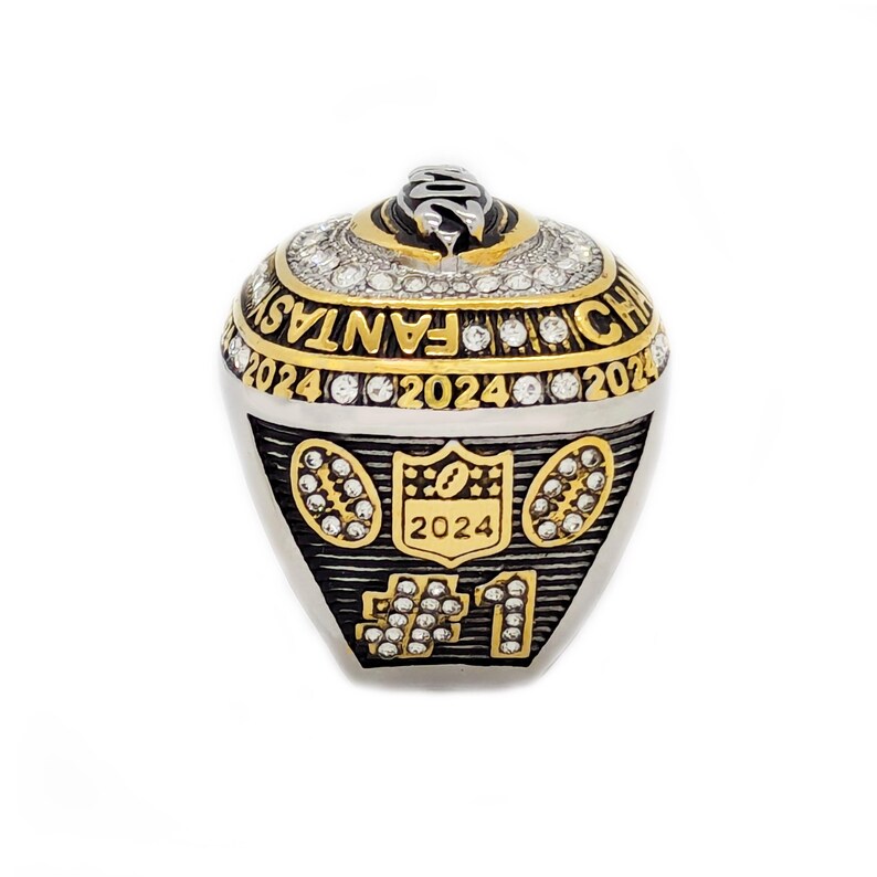 May include: A silver and gold ring with the text "2024 FANTASY CHAMP" and the number "#1". The ring has a football theme with the NFL logo and is encrusted with clear gemstones.